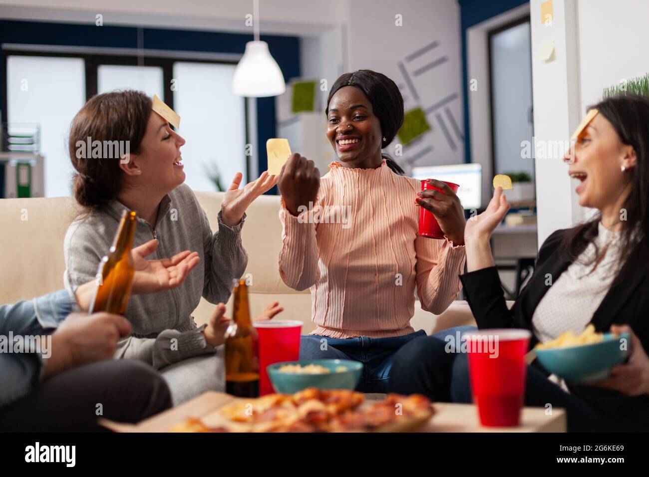 Une équipe diversifiée de collègues jouent à la devine après le travail au bureau tout en étant assis sur un canapé. Femme afro-américaine faisant l'usurpation d'identité pour le plaisir amusant d'activité de divertissement Banque D'Images