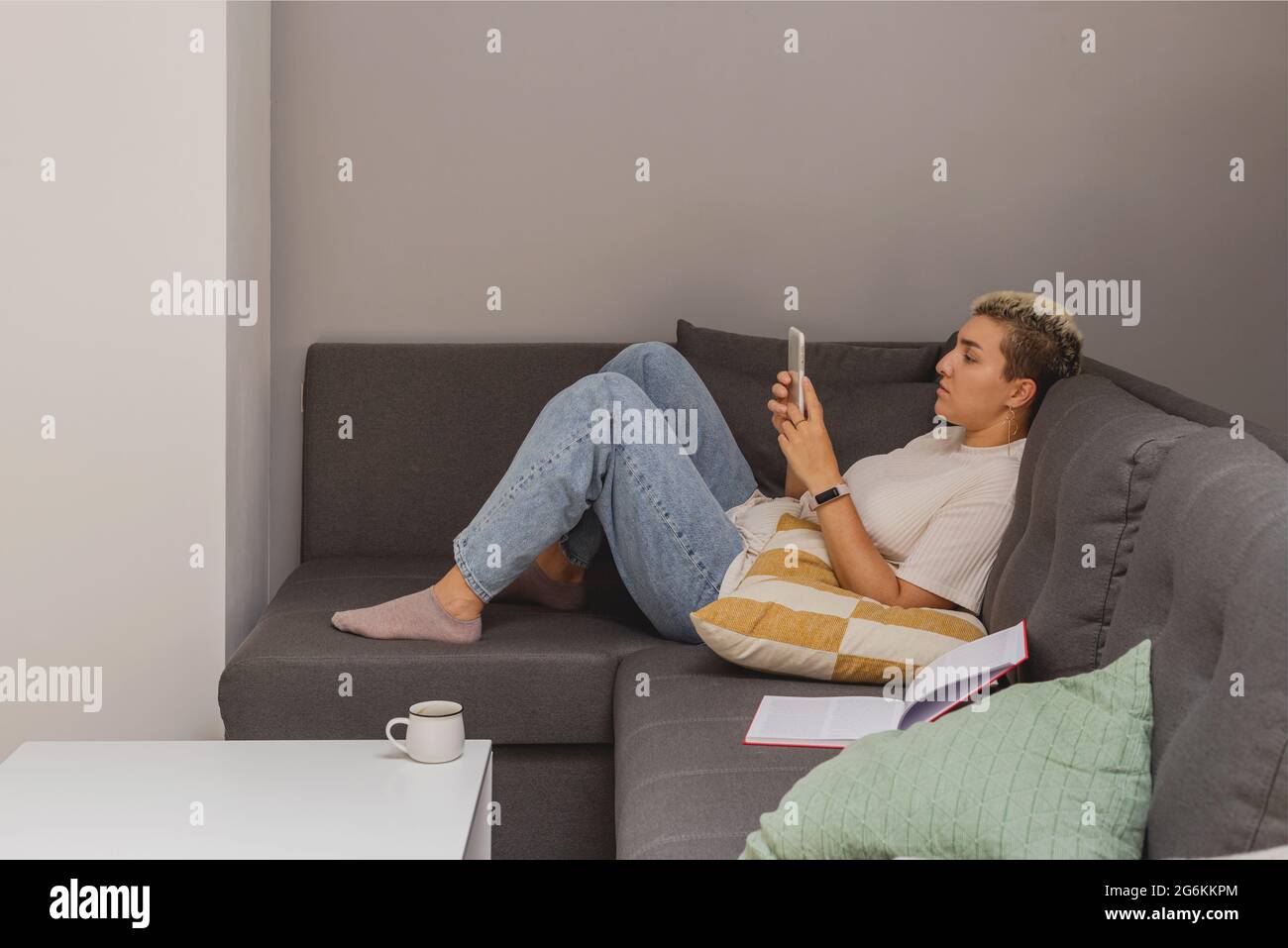 Une femme se trouve sur un canapé avec un smartphone dans un intérieur minimaliste. Banque D'Images