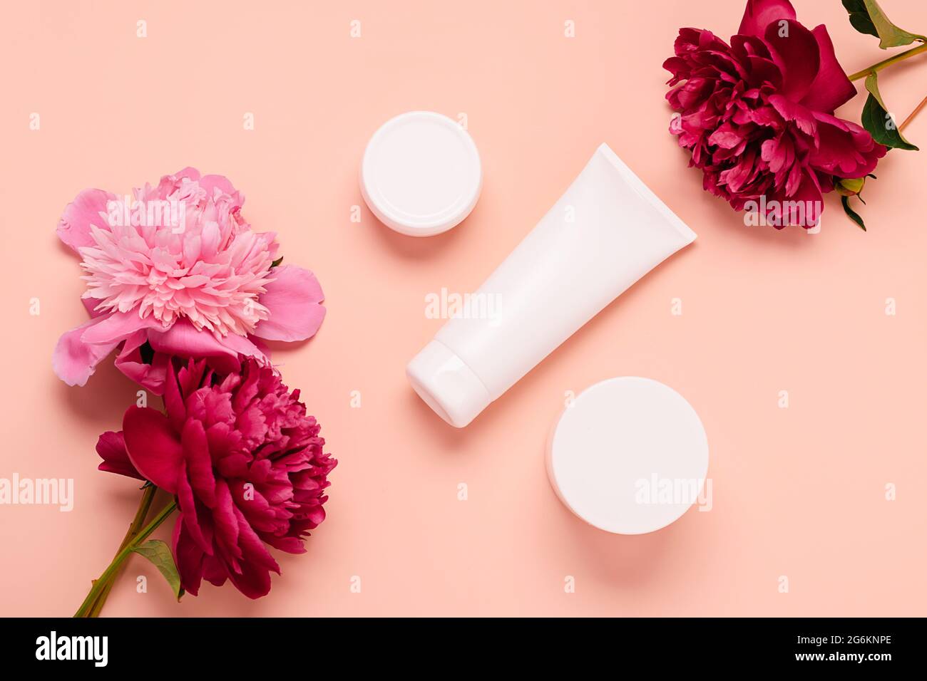 Produits cosmétiques crème gel shampooing baume dans différentes bouteilles sur fond rose avec fleurs fraîches pivoines Banque D'Images