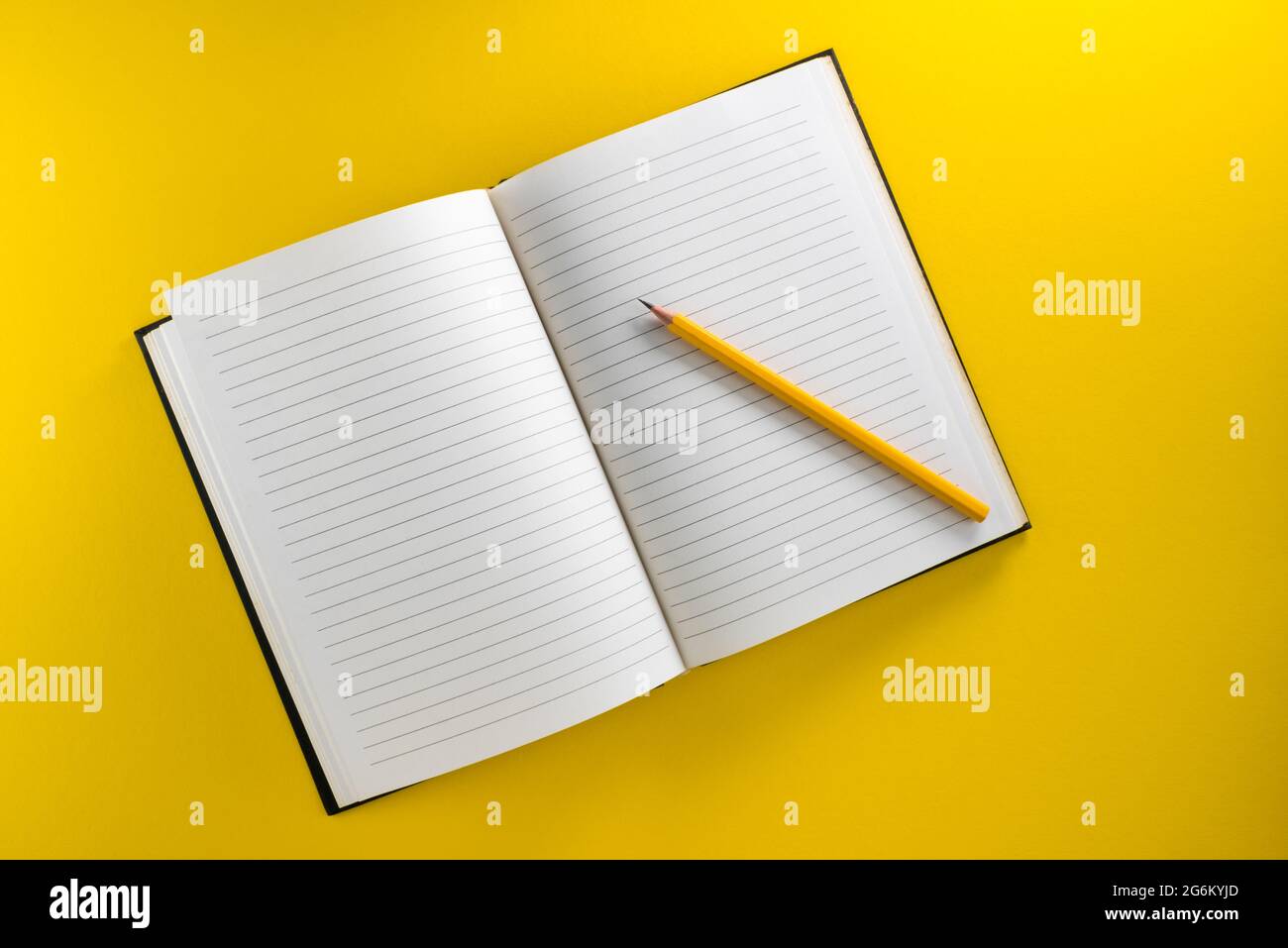 Cahier à lignes ouvertes avec crayon jaune isolé sur fond jaune dans la vue de dessus, plan à plat, espace de copie Banque D'Images
