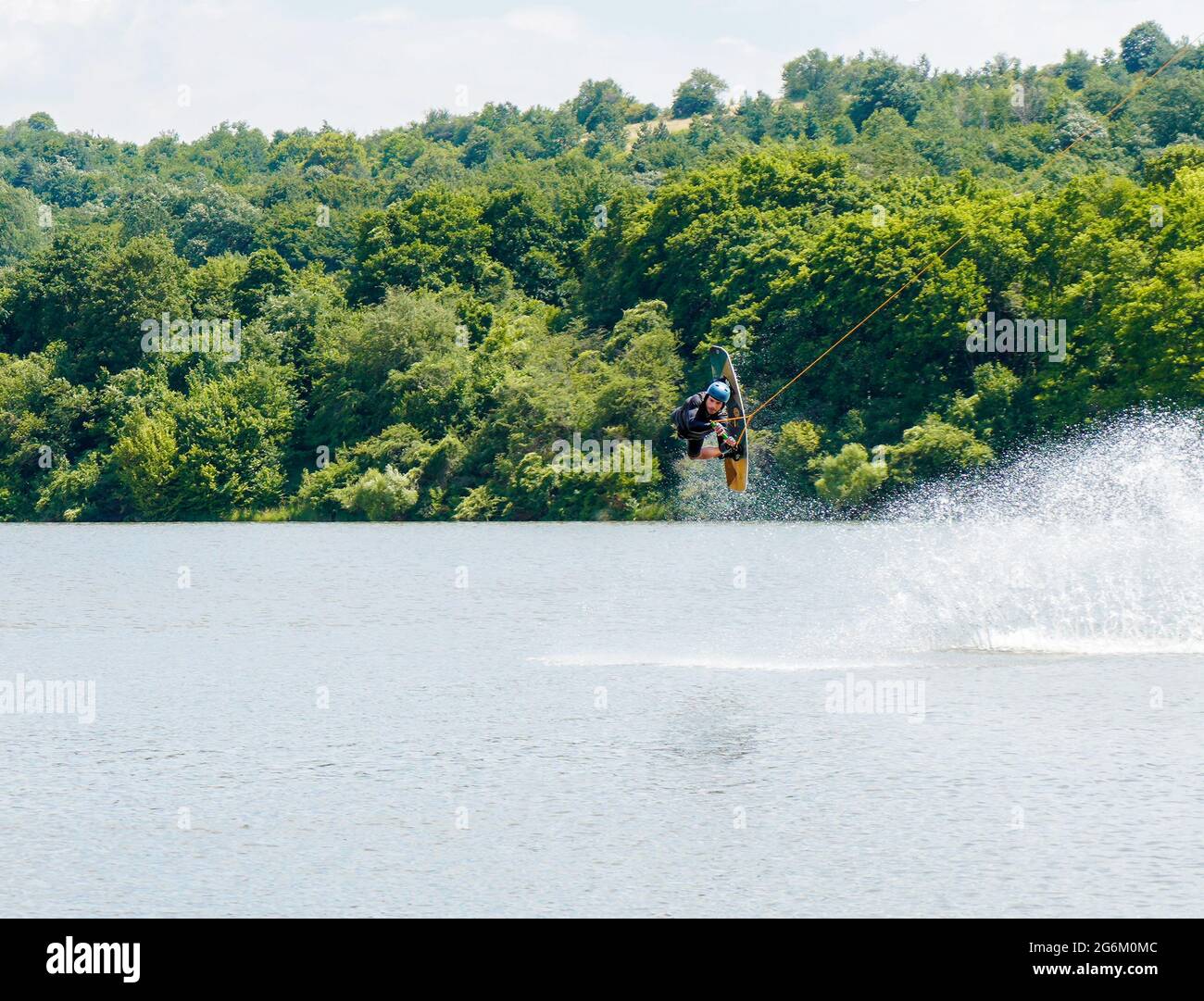 Homme faisant des cascades en wakeboarding dans la rivière contre les collines vertes pendant la journée ensoleillée Banque D'Images