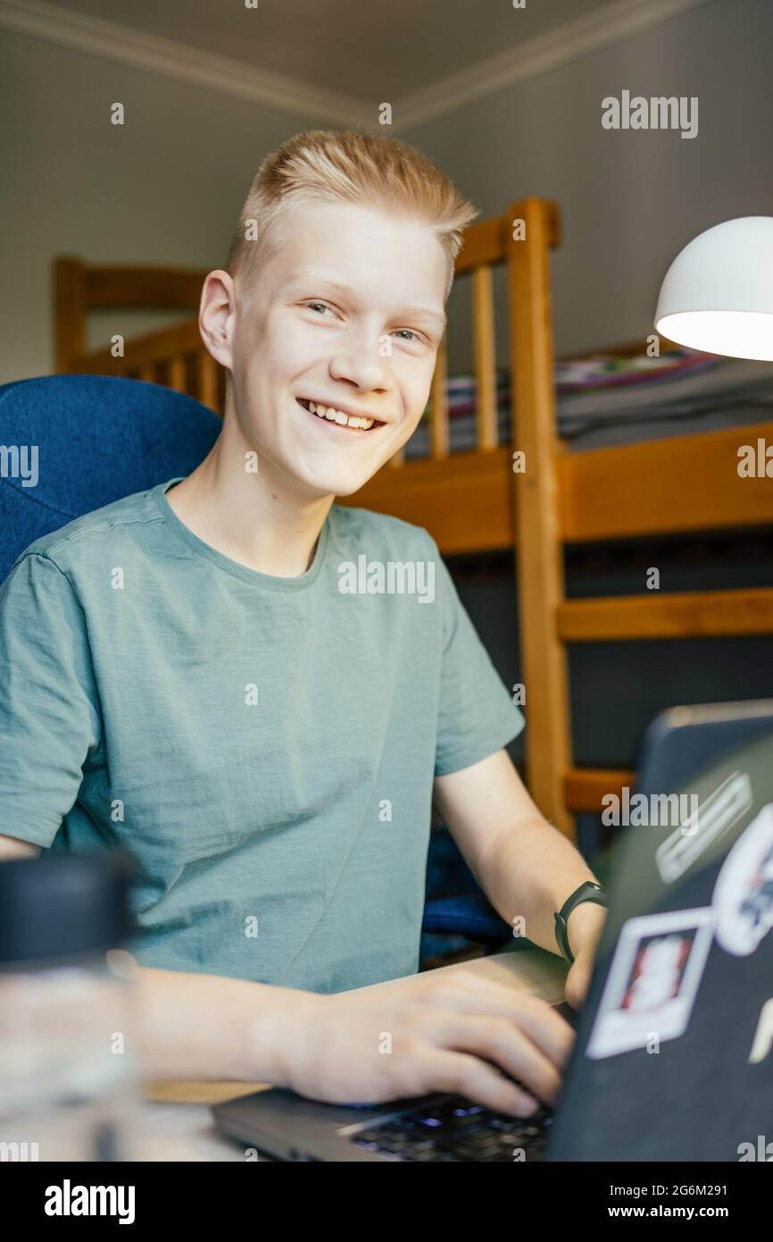 Le jeune homme est souriant et regarde la caméra tout en travaillant en ligne. Banque D'Images