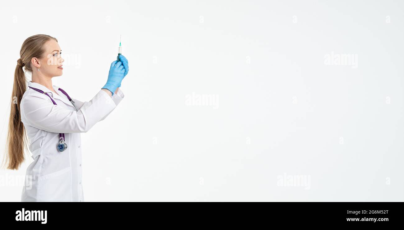 Une jeune infirmière dans un masque et un manteau blanc tient une seringue avec une aiguille pour les injections, les vaccins contre la grippe, le covid. Le concept de vaccination et de protection Banque D'Images