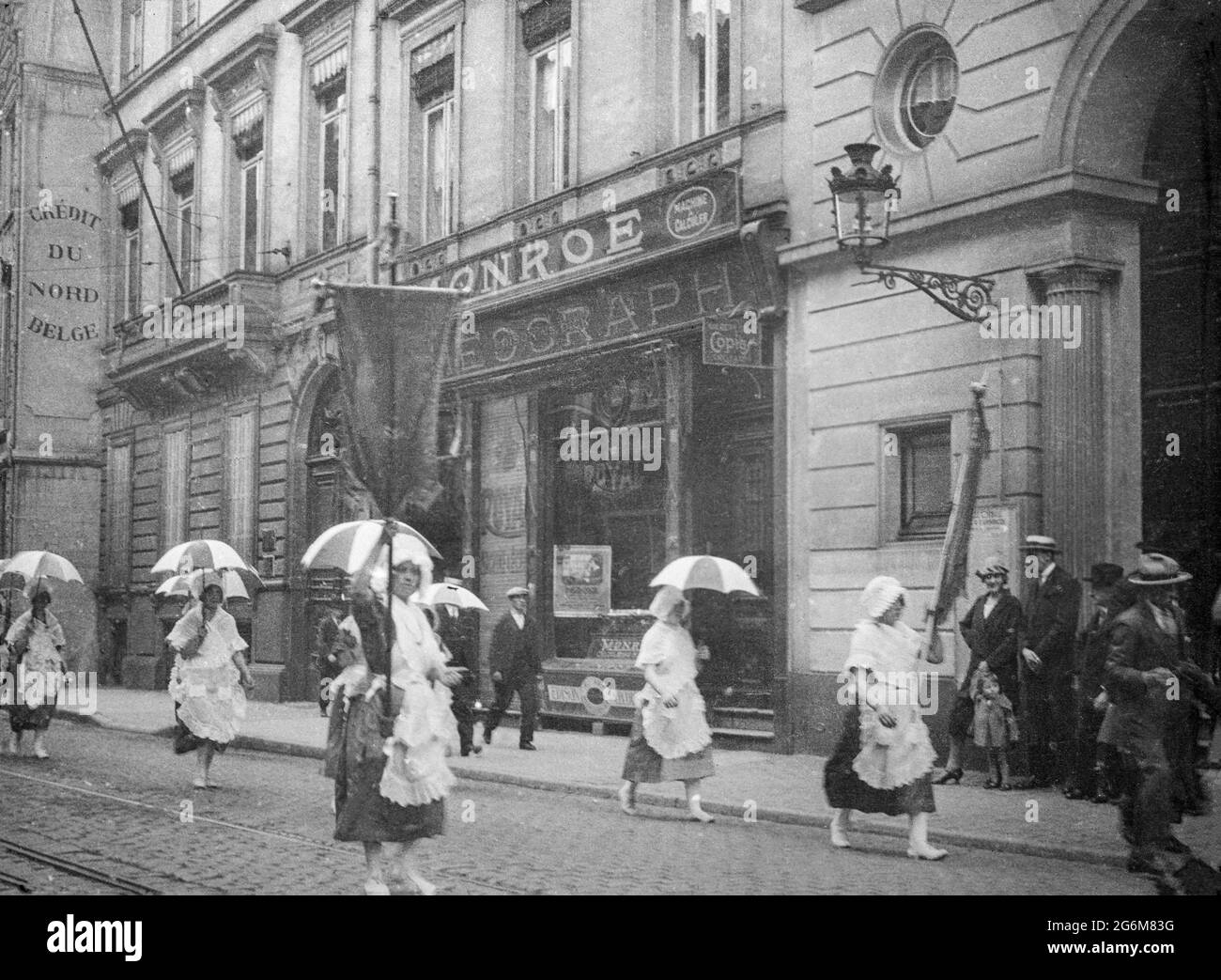 Une photographie ancienne en noir et blanc du début du XXe siècle prise à Bruxelles, en Belgique. L'image montre des femmes portant des parasols, marchant ou faisant une démonstration dans une rue. Banque D'Images