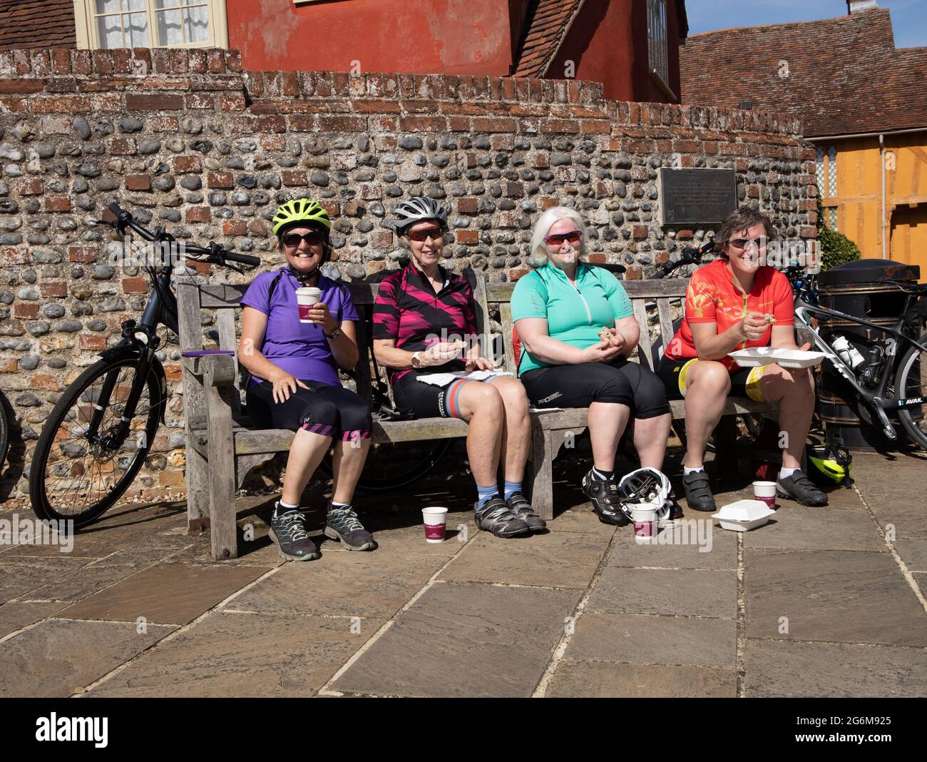 Quatre joyeuses femmes cyclistes mangeant et se reposant sur le banc Lavenham Suffolk Angleterre Banque D'Images