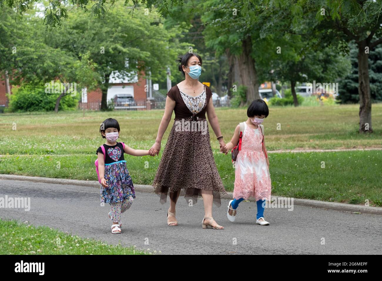 Une femme bien habillée et, vraisemblablement, ses enfants bien habillés, marchent dans un parc dans le Queens portant des masques chirurgicaux. Banque D'Images