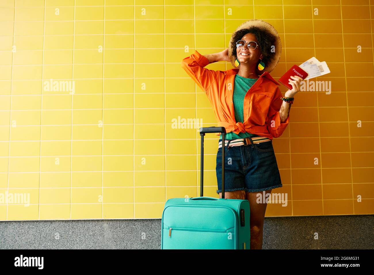 Belle femme élégante quittant sa maison en ville avec une valise pour aller en vacances, tenant un passeport international et un billet avia Banque D'Images