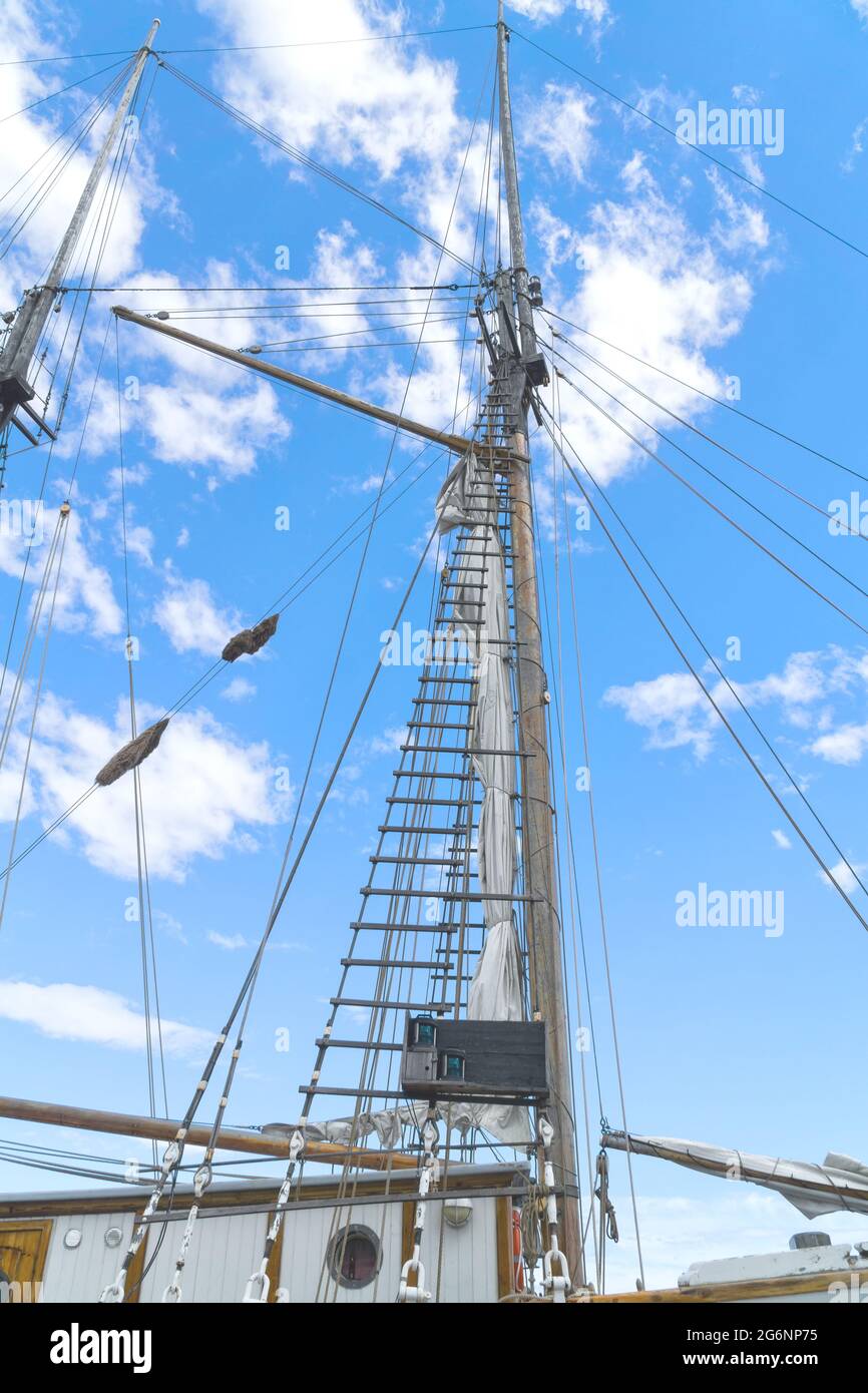 Mât en bois et cordes de voilier, vue des mâts du navire par le dessous, gréement détaillé sans voiles contre ciel bleu avec nuages blancs. Banque D'Images