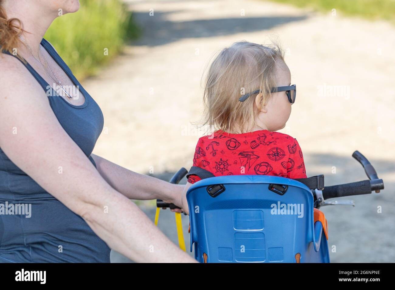 Vue arrière d'un petit garçon assis sur un siège de vélo sans casque de sécurité. Sa mère tient un vélo. Banque D'Images