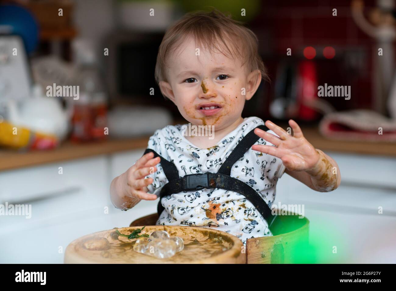 Un bébé mangeant du désordre dans une chaise haute Banque D'Images