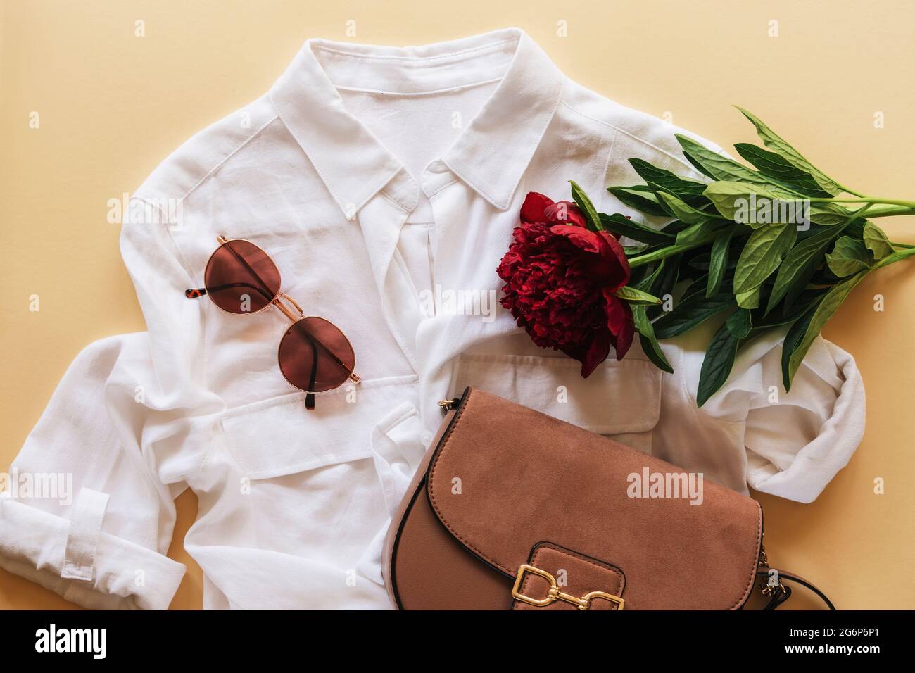 Femme mode plat vêtements décontractés avec blouse blanche, sac à main, lunettes de soleil et fleur de pivoine rouge foncé sur fond beige. Vue de dessus Banque D'Images