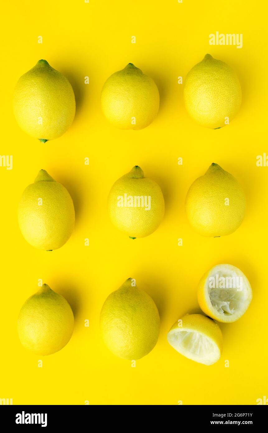 9 citrons alignés, un coupé et pressé, sur fond jaune Banque D'Images