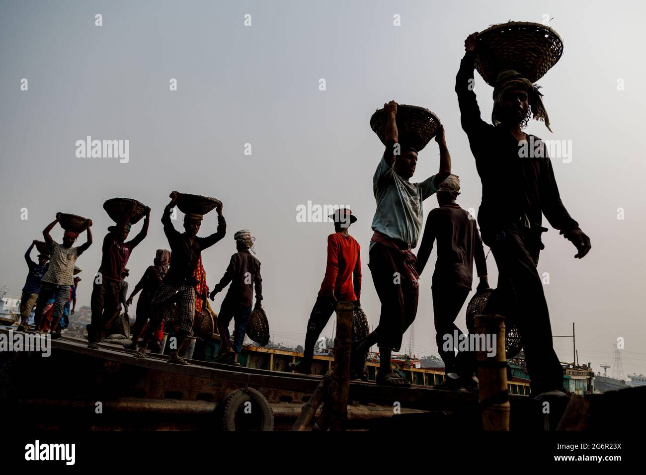 Une chaîne humaine de porteurs transporte du charbon, du sable et du gravier depuis les barges amarrées à la station d'atterrissage d'Aminbazar, sur le fleuve Buriganga, à l'extérieur de Dhaka. Le Bangladesh est diplômé de la catégorie des PMA (pays les moins avancés), grâce en grande partie au travail extrêmement difficile de la main-d'œuvre manuelle bon marché. Un porteur fait entre 80 et 140 USD par mois, selon les sites paylab.com et averagesalarysurvey.com Banque D'Images