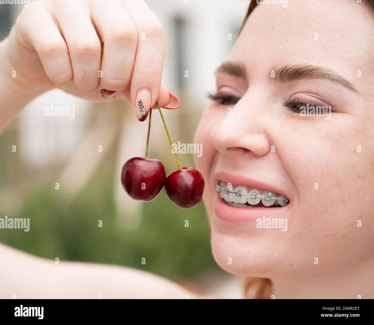 Belle jeune femme aux cheveux rouges avec des bretelles sur ses dents mange  des cerises douces en plein air en été Photo Stock - Alamy
