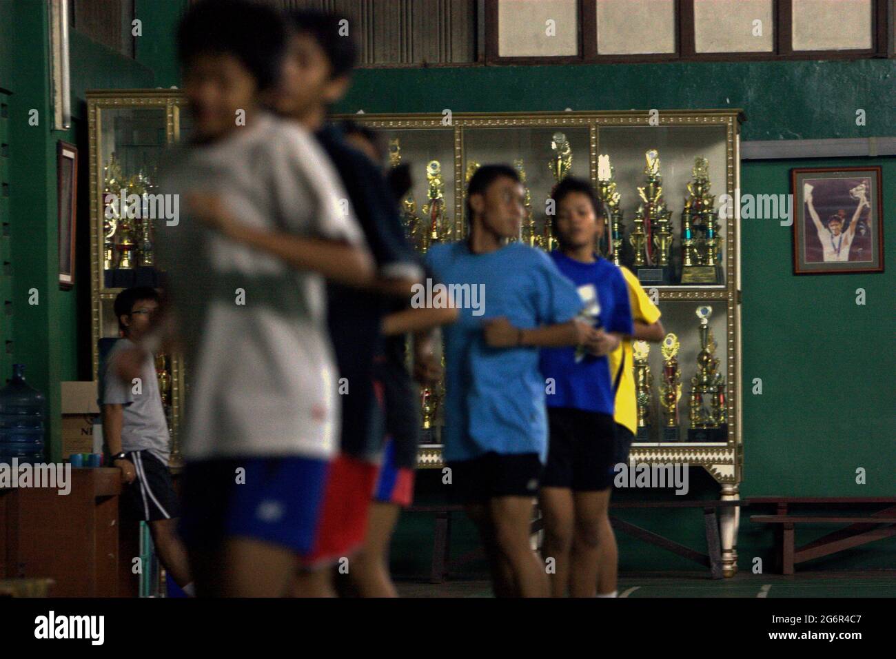 De jeunes joueurs de badminton se réchauffent lors d'une séance d'entraînement au club de badminton Jaya Raya à Jakarta, en Indonésie, photographiés dans un fond d'armoire à trophées et une photo de l'ancien joueur vedette du club, Susi Susanti, médaillé d'or olympique. Banque D'Images
