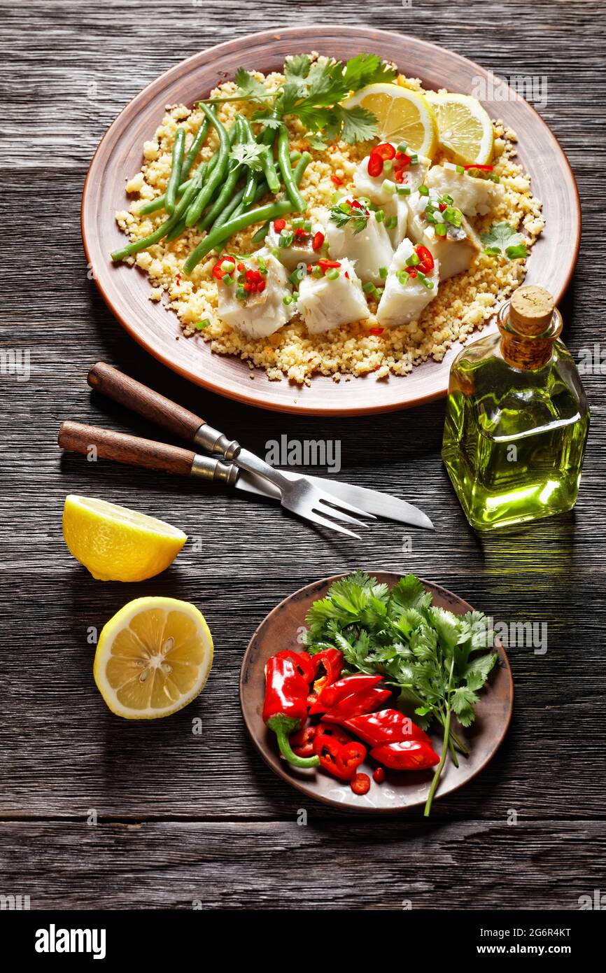 Bacalhau com todos, morue au bulgur, haricots verts cuits à la vapeur, saupoudrée de piments forts et d'oignons de printemps sur une assiette rustique, sur une table en bois, por Banque D'Images