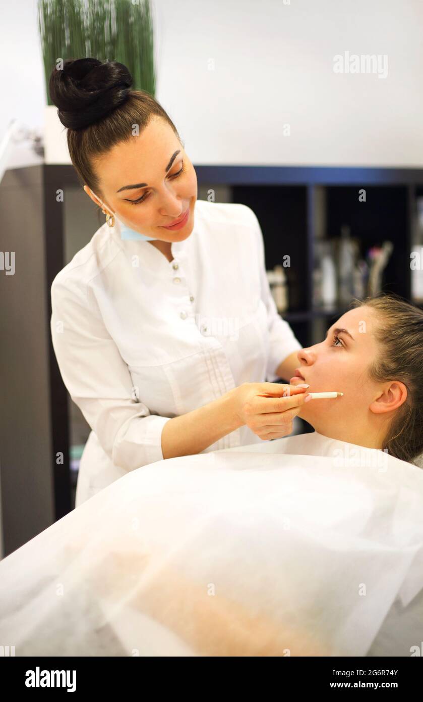 Esthéticienne féminine en robe blanche ligne de dessin sur le visage de la femme pendant le travail dans la clinique de cosmétologie Banque D'Images