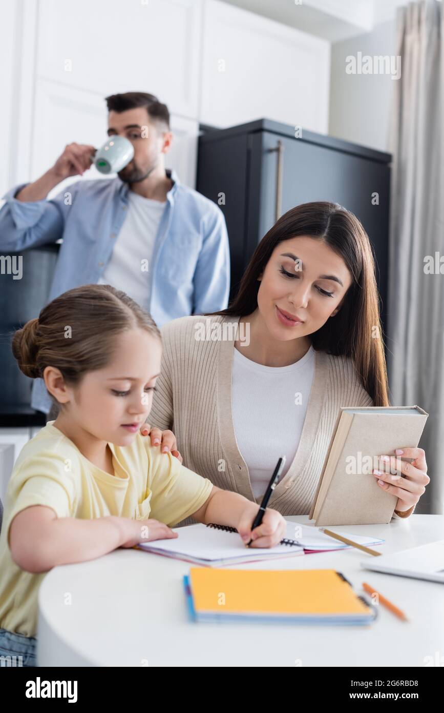 un homme flou buvant un café près de sa fille faisant ses devoirs avec sa mère Banque D'Images