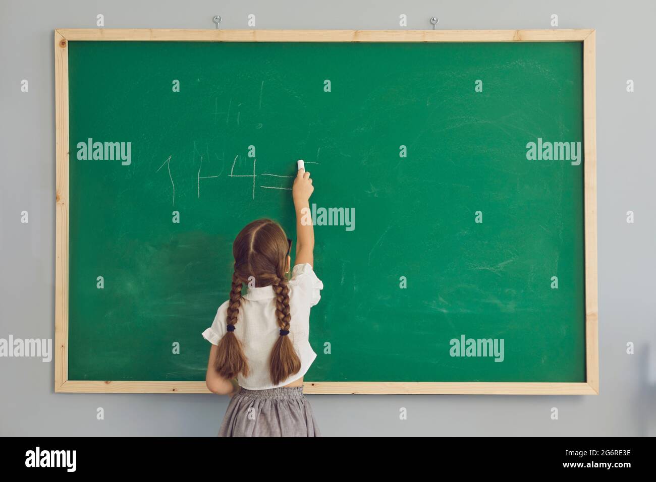 Vue arrière de la petite fille étudiante écrivant vers le bas somme arithmétique vert école tableau de surveillance Banque D'Images