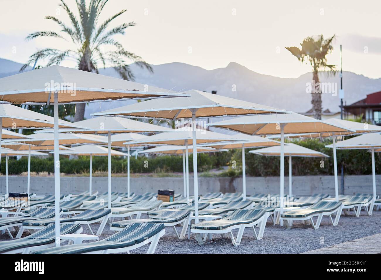 Plage vide le soir avec vue magnifique sur les mountais et les palmiers. Parasols et chaises longues au coucher du soleil près de la mer Méditerranée. Plage de galets. Photo de haute qualité Banque D'Images