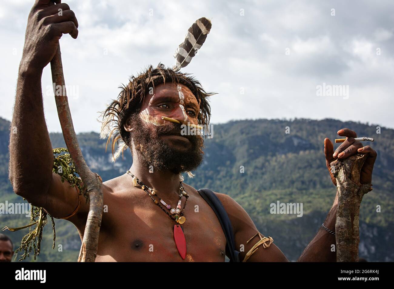 Un guerrier de tribu avec un grand nez de tusk piquant en fumant une cigarette. PAPOUASIE OCCIDENTALE, INDONÉSIE : en une seule image, quatre guerriers étaient assis sur le groun recouvert de paille Banque D'Images