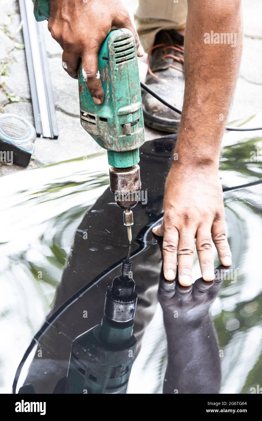 Ouvrier perçant la tôle de polycarbonate de toit avec la vis sur le cadre de structure Banque D'Images