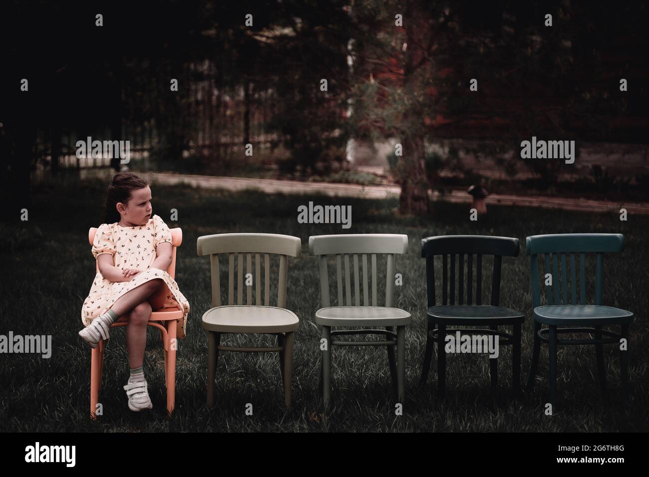 une fille solitaire, triste dans une robe s'assoit sur une rangée vide de chaises dans l'arrière-cour des outdoots et pleure que personne n'est venu à son anniversaire Banque D'Images