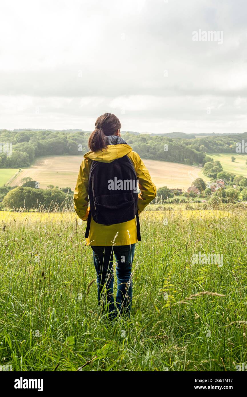Femme marchant avec une veste jaune et un sac à dos en profitant de la vue sur la campagne et en regardant les Sussex Downs. Banque D'Images