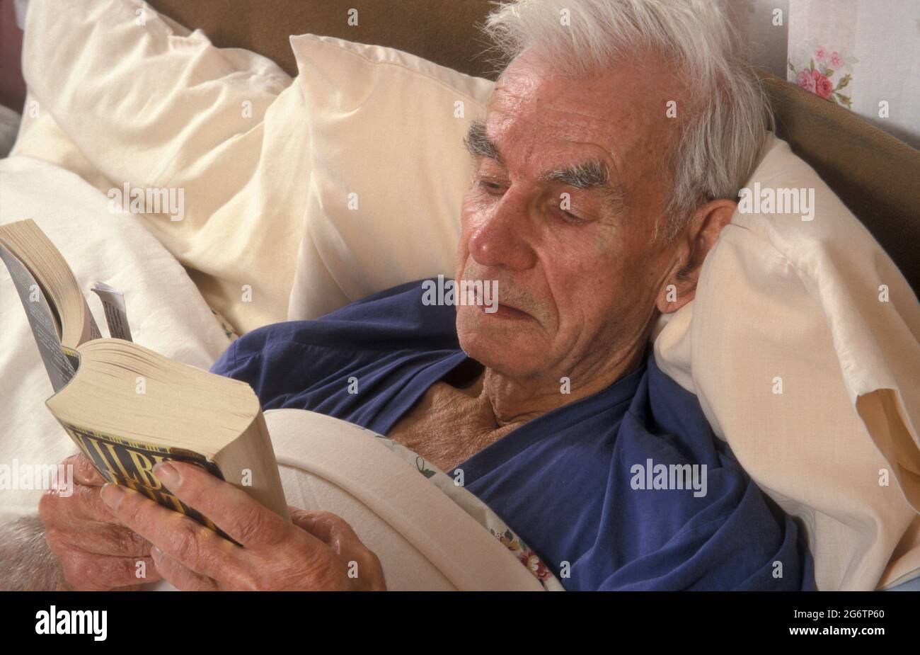 homme âgé au lit lisant un livre Banque D'Images