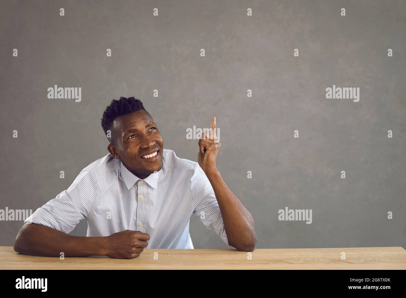 Joyeux jeune homme noir assis au bureau et pointant le doigt vers le haut à l'espace de copie publicitaire Banque D'Images