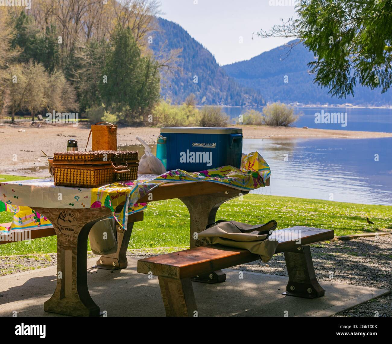 Table en bois avec boîtes et paniers de nourriture pour le pique-nique en plein air dans un parc sur le fond du lac et des montagnes. Harrison Lake, C.-B., Canada. A Banque D'Images