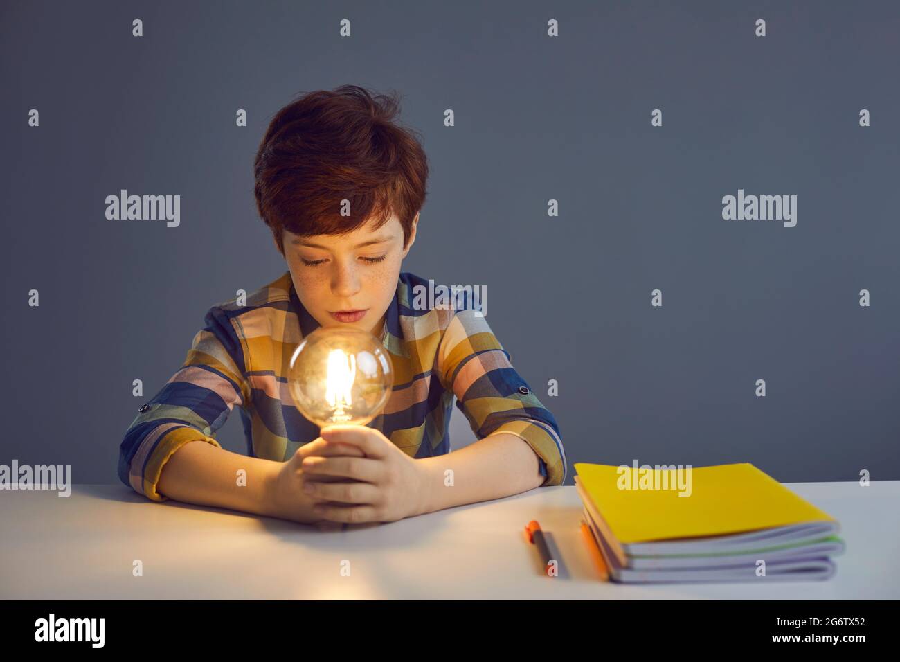 Petit garçon enfant assis à la table de l'école et regardant l'ampoule lumineuse Banque D'Images