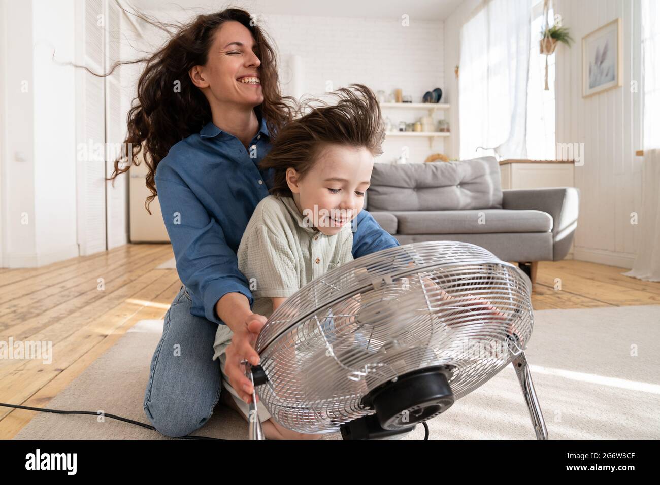 Famille ensemble: Jeune maman et fils d'âge préscolaire rire assis au ventilateur soufflant vent frais dans le visage Banque D'Images