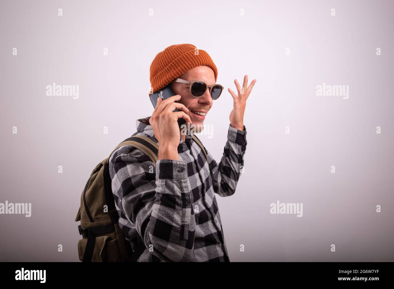 Un homme élégant fait un appel téléphonique, il porte une chemise à carreaux, des lunettes de soleil et une casquette, un boxer avec sac à dos, photo prise dans le studio avec fond blanc Banque D'Images