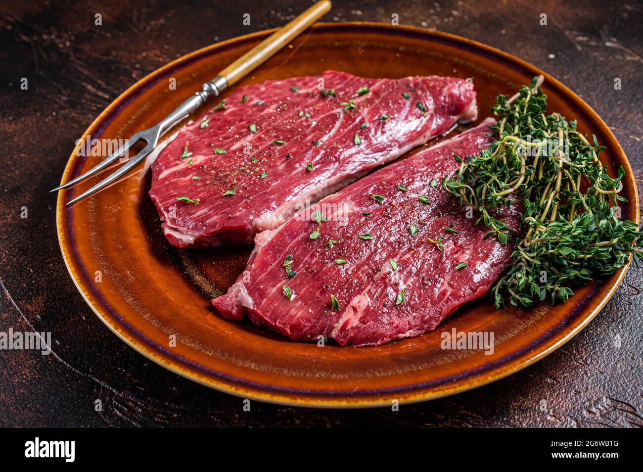 Steak de calotte cru ou steak d'aloyau dans une assiette rustique au thym et à l'huile d'olive. Arrière-plan sombre. Vue de dessus Banque D'Images