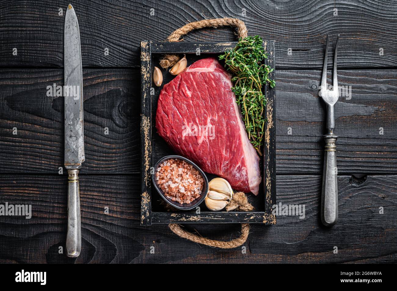 Steak de viande de bœuf coupé au sommet de la sirloine crue ou Picanha dans un plateau en bois avec des herbes. Arrière-plan en bois noir. Vue de dessus Banque D'Images