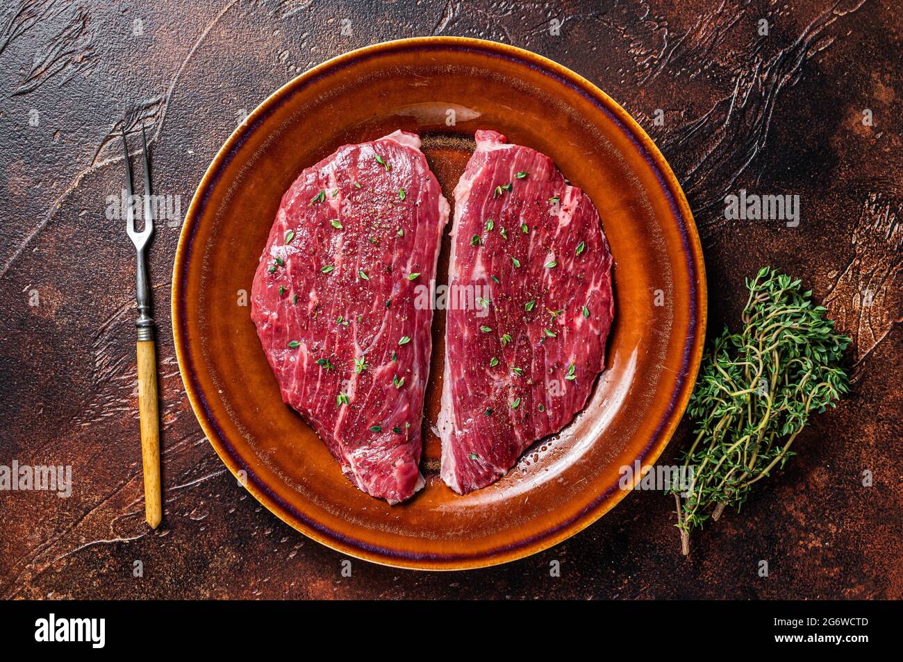 Steak de calotte cru ou steak d'aloyau dans une assiette rustique au thym et à l'huile d'olive. Arrière-plan sombre. Vue de dessus Banque D'Images