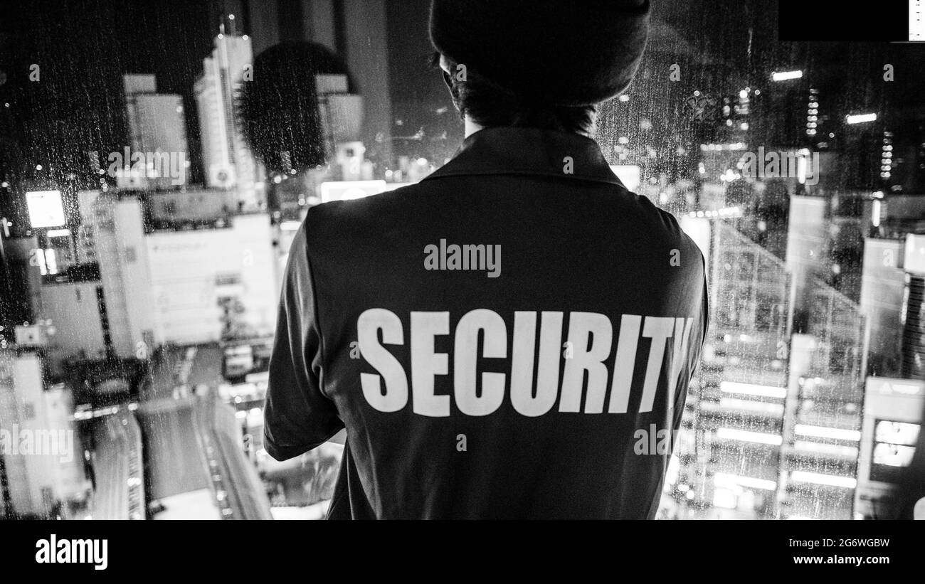 Image monochrome d'un agent de sécurité qui regarde la ville la nuit à Tokyo, au Japon Banque D'Images