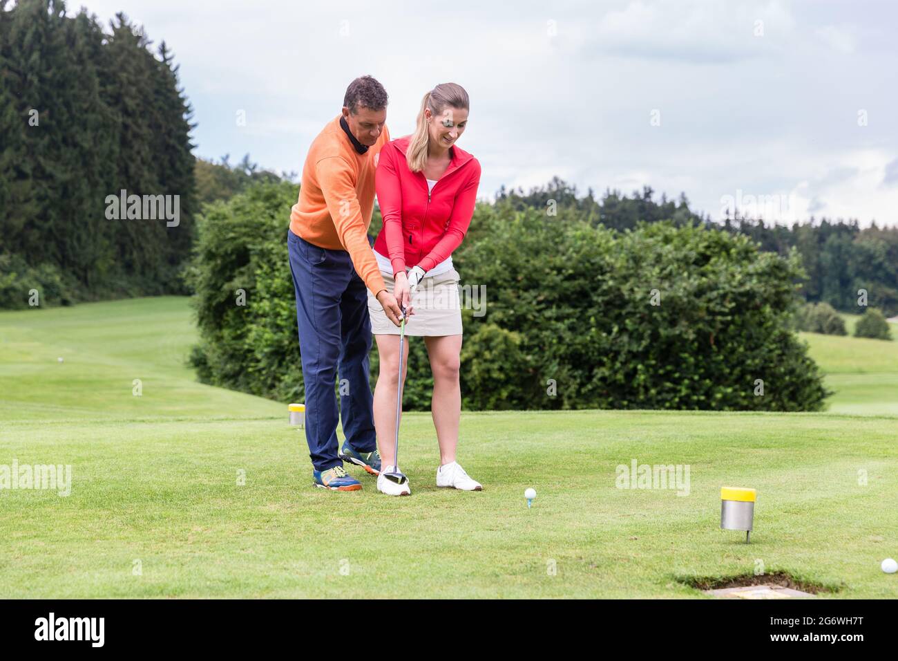 Homme enseignant à la femme de jouer au golf en se tenant sur le terrain Banque D'Images