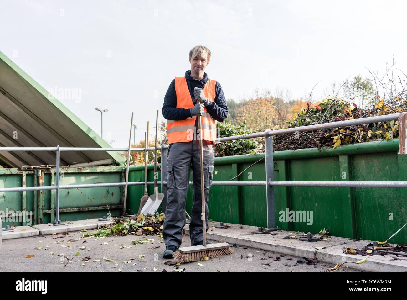 Homme balayant le sol du centre de recyclage après avoir placé le vert de déchets dans le conteneur Banque D'Images