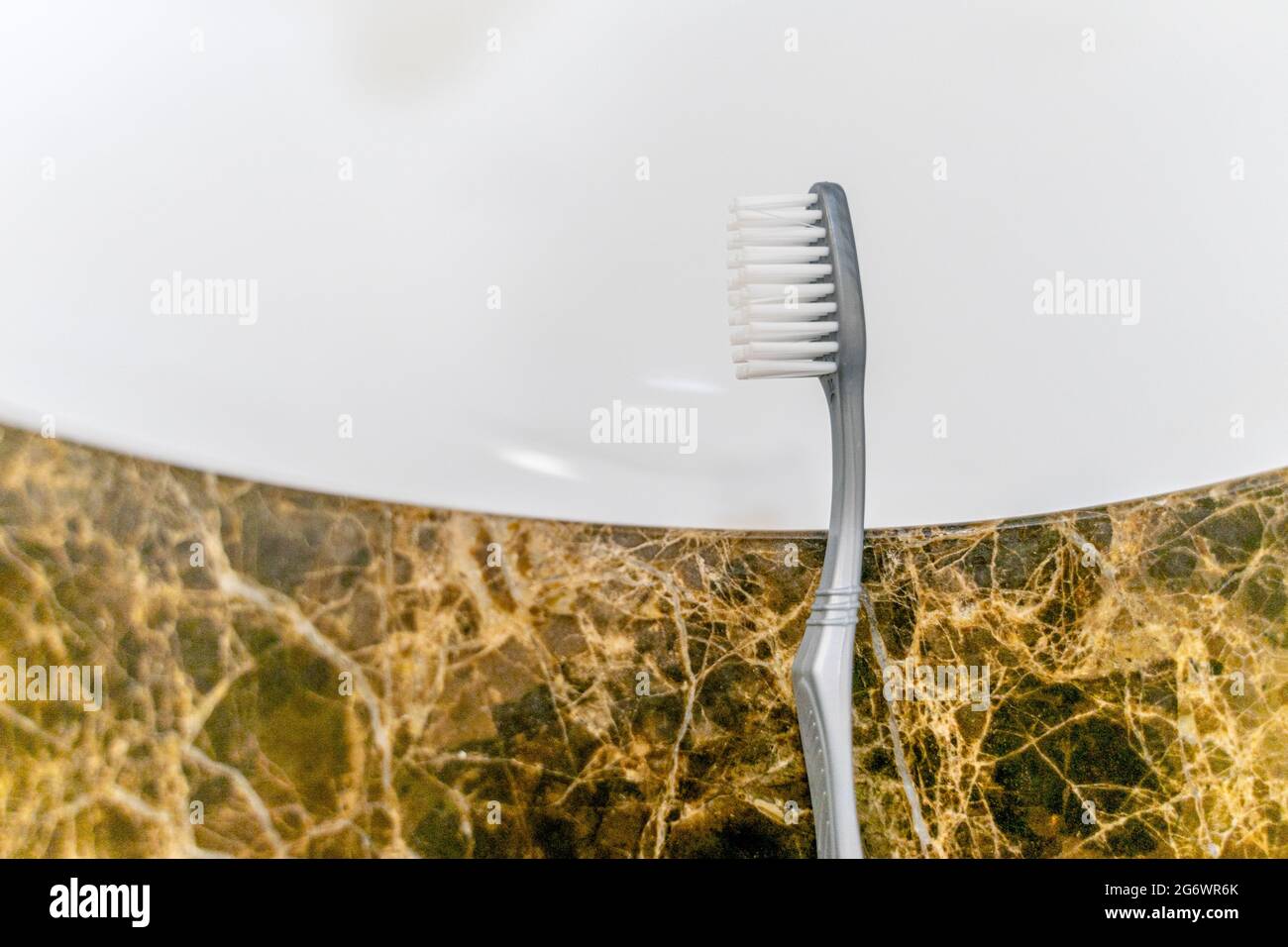 Tête de brosse à dents reposant sur le bord d'un évier blanc sur un support en marbre. Banque D'Images