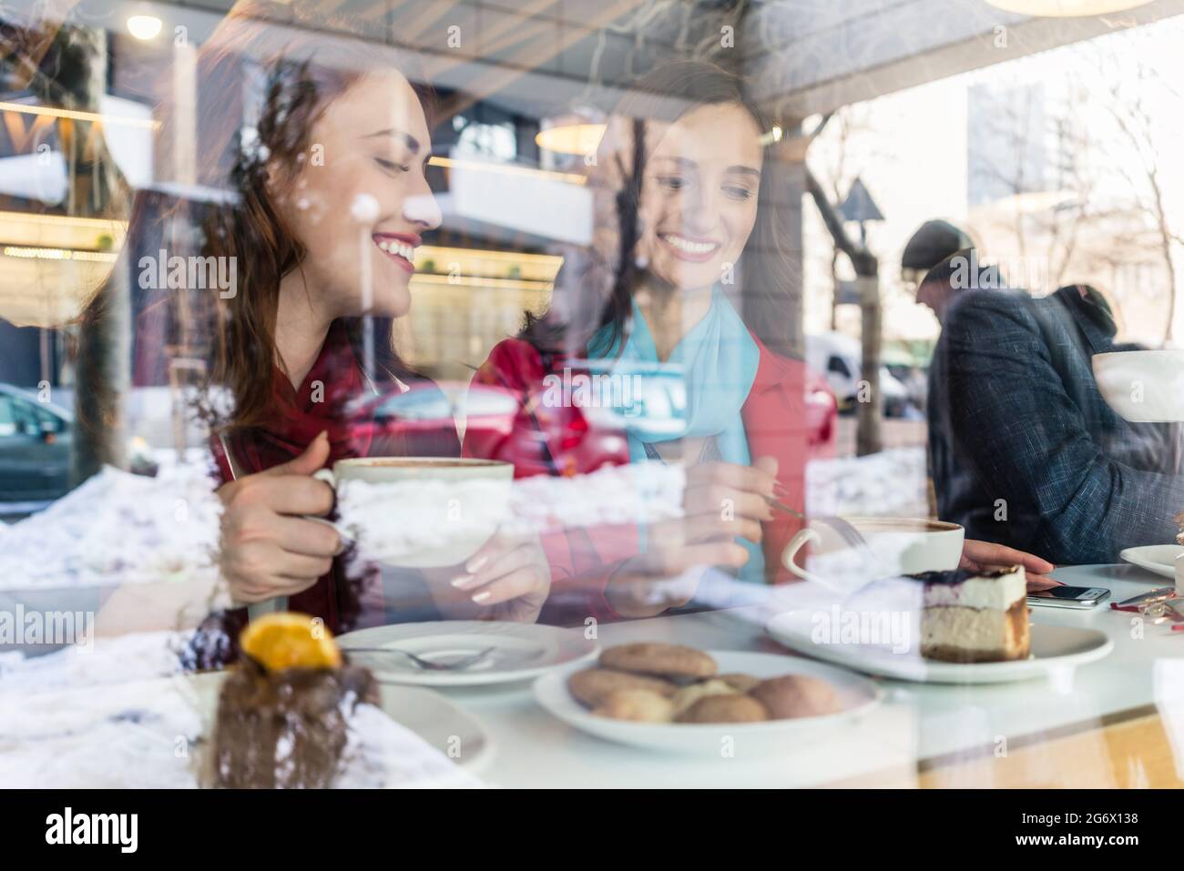 Deux jeunes et belles femmes souriant tout en dégustant ensemble de délicieux gâteaux et café dans un café branché du centre-ville Banque D'Images