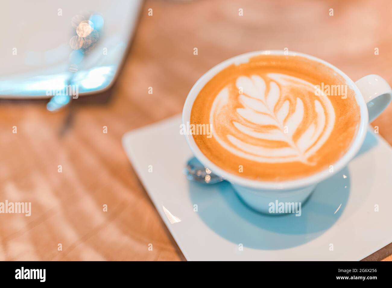 Latte dans une tasse de cappuccino à la table du café. Gros plan de la fleur de rosetta dessinant dans la mousse. Tasse à café blanche en gros plan avec latte en forme de coeur Banque D'Images