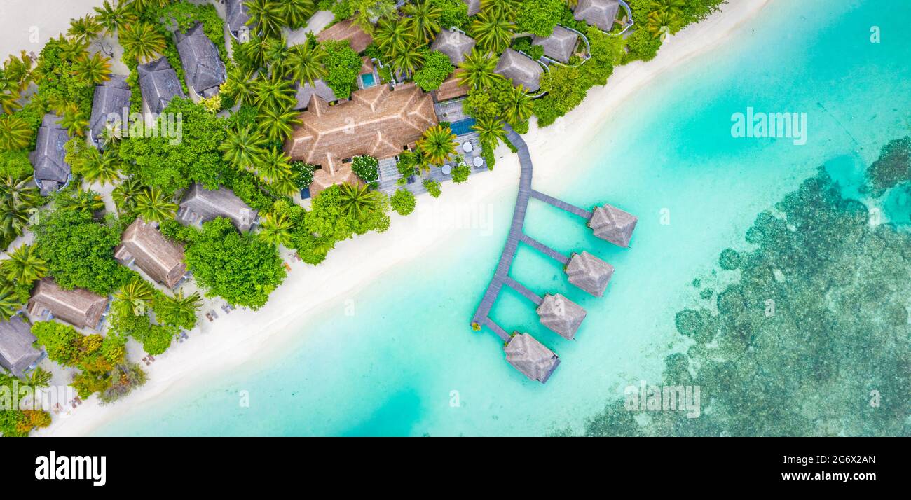 Paysage aérien de drone vue bleu eau et pont en bois et villas d'eau avec île paradisiaque rive, mer côte palmier. Des voyages aériens époustouflants Banque D'Images