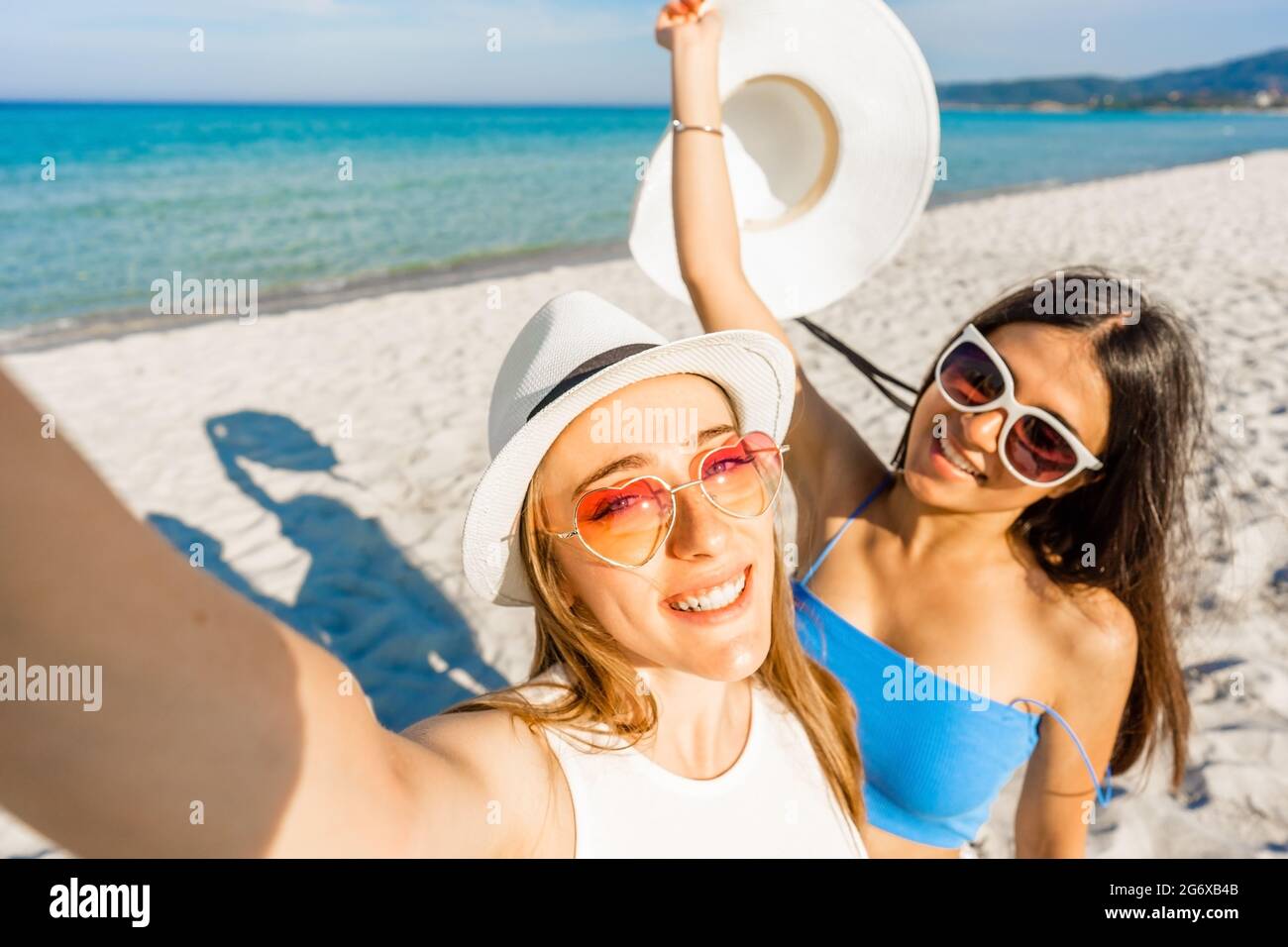 Deux belles filles avec des chapeaux blancs prenant un autoportrait  appréciant les vacances d'été sur la plage tropicale station. POV de la  jeune femme blonde utilisant smartpho Photo Stock - Alamy