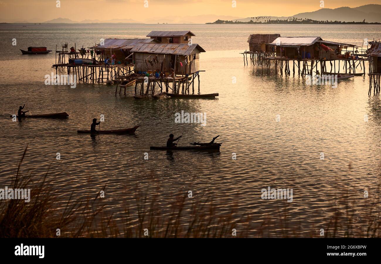 Les gens de Bajau Laut qui pagayent à la maison de leurs pilotis au coucher du soleil Banque D'Images