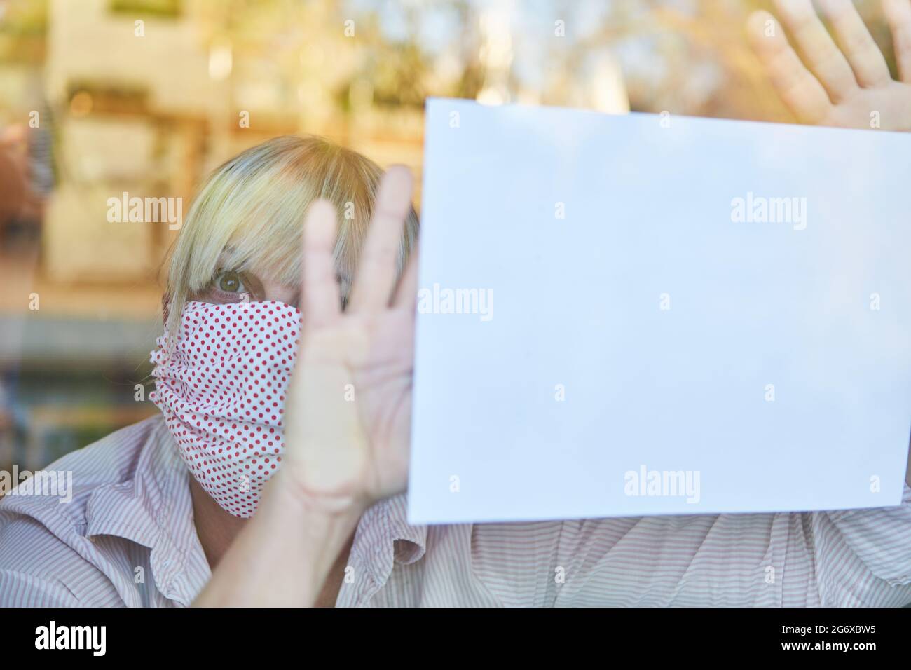 Une femme solitaire âgée avec masque de quarantaine continue à pleurer pour obtenir de l'aide à la fenêtre pendant une pandémie de coronavirus Banque D'Images