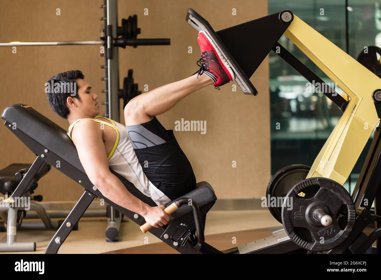 Longueur pleine vue de côté d'un jeune homme fort et de l'exercice à la  presse jambes la machine lors de la routine d'entraînement du bas du corps  dans la salle de sport