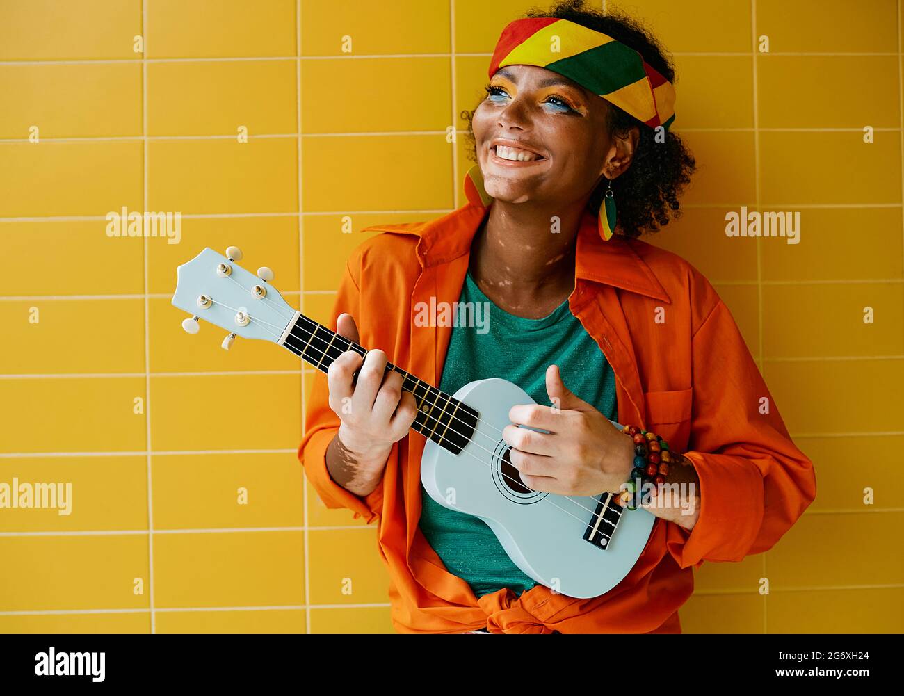 Amusant rastafarian femme jouant bleu ukulele près du mur jaune. Musicienne de rue Banque D'Images