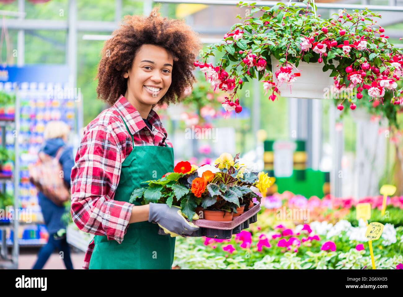 Portrait d'une jeune femme gaie portant un tablier vert et des gants de jardinage tout en travaillant avec dévouement comme fleuriste dans un magasin de fleurs moderne Banque D'Images